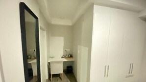 A room with a white wardrobe, a desk with a chair, and a mirror.