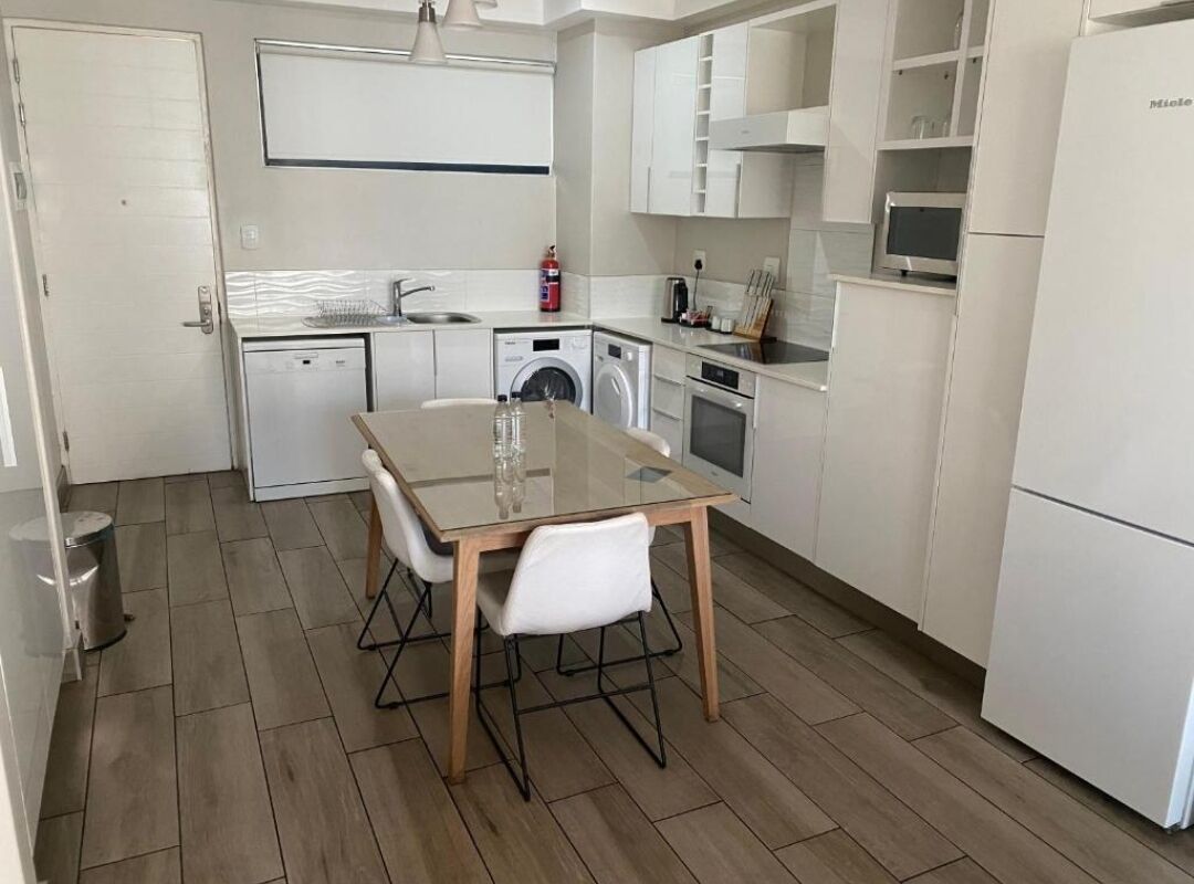 A compact kitchen with a dining table, washing machine, microwave, and a refrigerator.