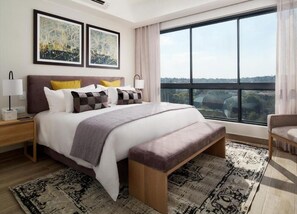 Ein modernes Schlafzimmer mit einem großen Bett, Nachttischen, einer Bank und Blick auf die Stadt durch große Fenster.