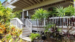 A covered porch with a white railing, surrounded by various potted plants and a small staircase leading to the entrance. - Koana's Ocean Hale Onsite Pool (Kailua-Kona)