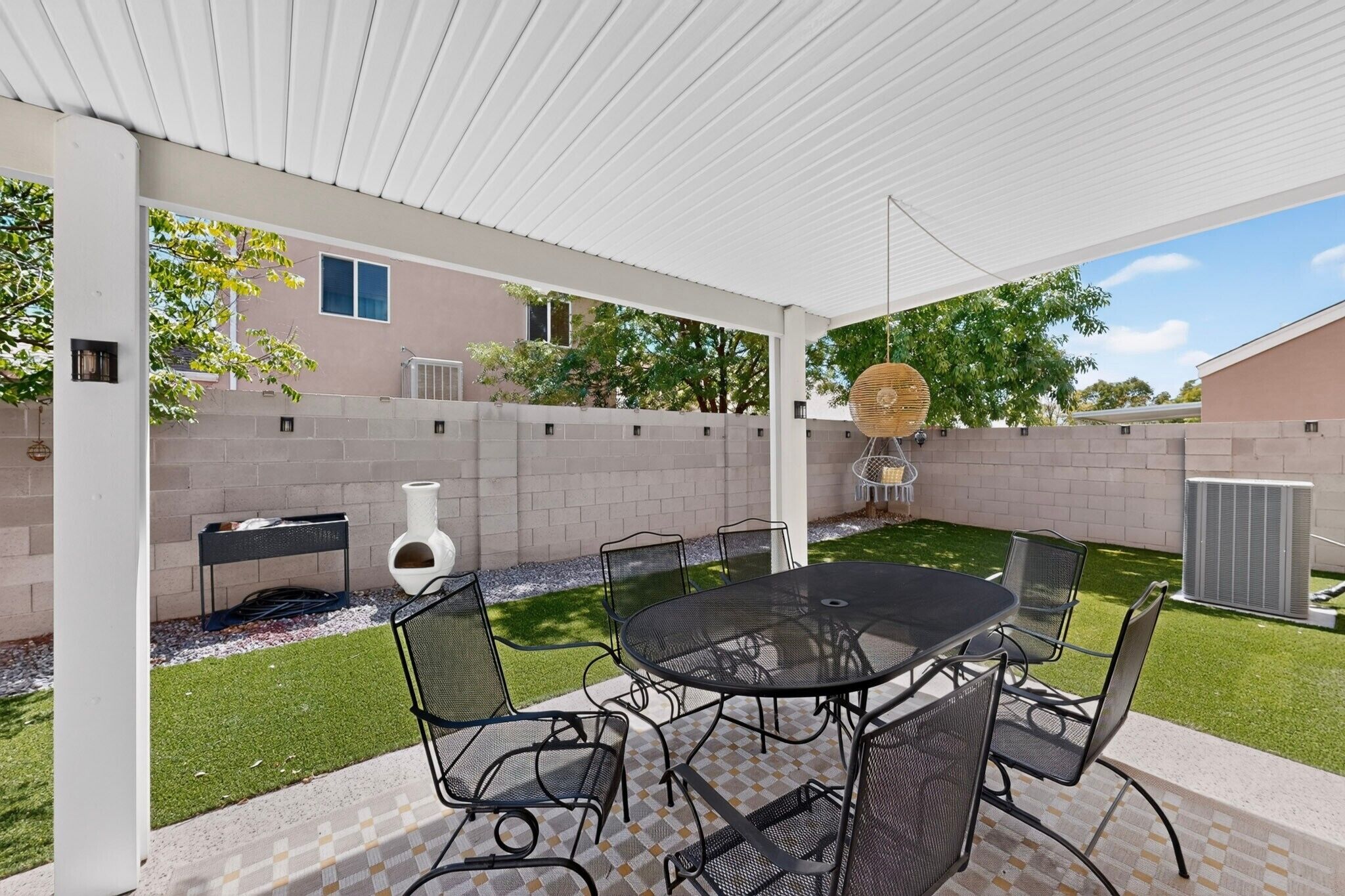 A covered patio with a table and chairs, a decorative vase, and a grill.