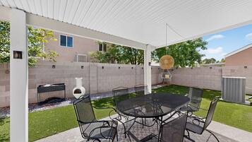 A covered patio with a table and chairs, a decorative vase, and a grill.