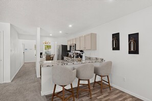 A modern kitchen with a marble countertop, wooden cabinets, and a central island with bar stools. - Peaceful 3bd/2.5ba home w/ yard, garage (Albuquerque)