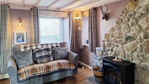 A cozy living room with a sofa, a fireplace, a stone wall, and a deer head decoration.