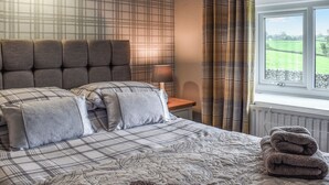A bedroom with a plaid-patterned bedspread, a headboard, and a view of a green field through a window.