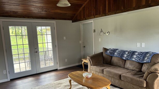 A living room with a brown couch, a wooden coffee table, and a white rug. There are two white doors with glass panels, a ceiling fan, and a light fixture.