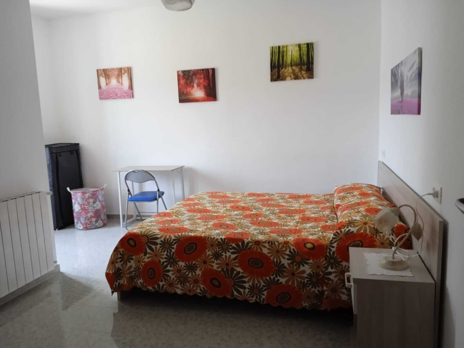 Una camera da letto con un letto, una sedia, una scrivania e tre quadri appesi al muro.
