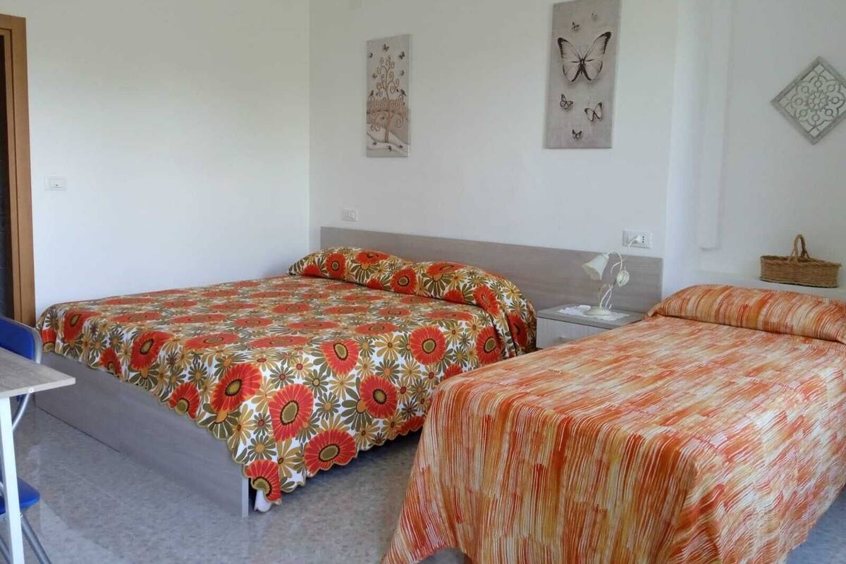 A room with two single beds, a small desk, and a chair. There are wall decorations including a butterfly and a geometric pattern.