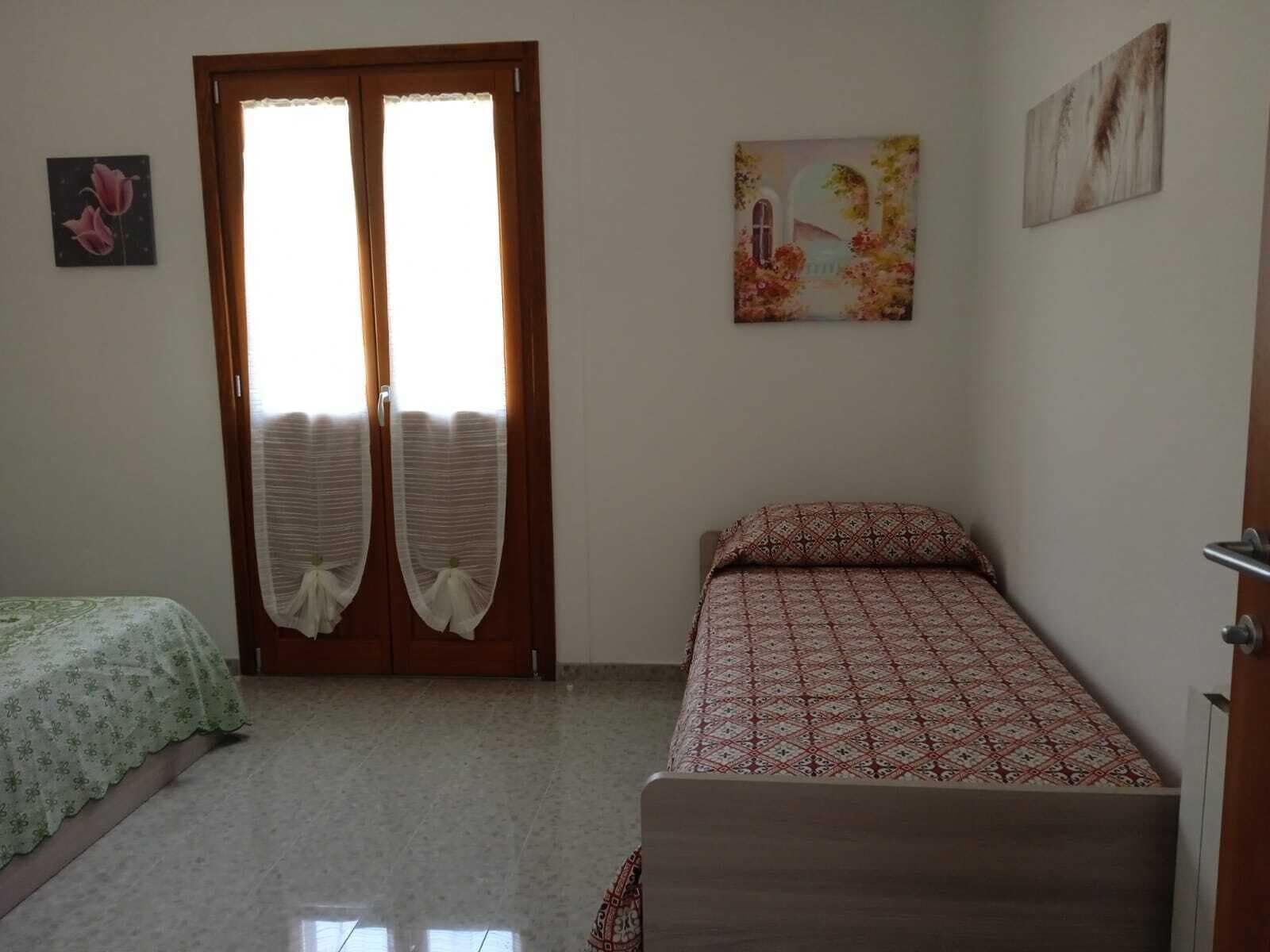 A bedroom with a bed, a small table, a door with curtains, and two wall-mounted pictures.