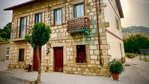 A two-story stone building with a balcony, a red door, and a small garden area with potted plants. - I 3 falchi Bed & Breakfast (Pennadomo)