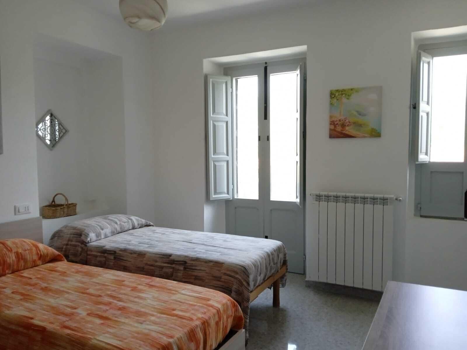 A bedroom with two beds, a radiator, and a window with open shutters.
