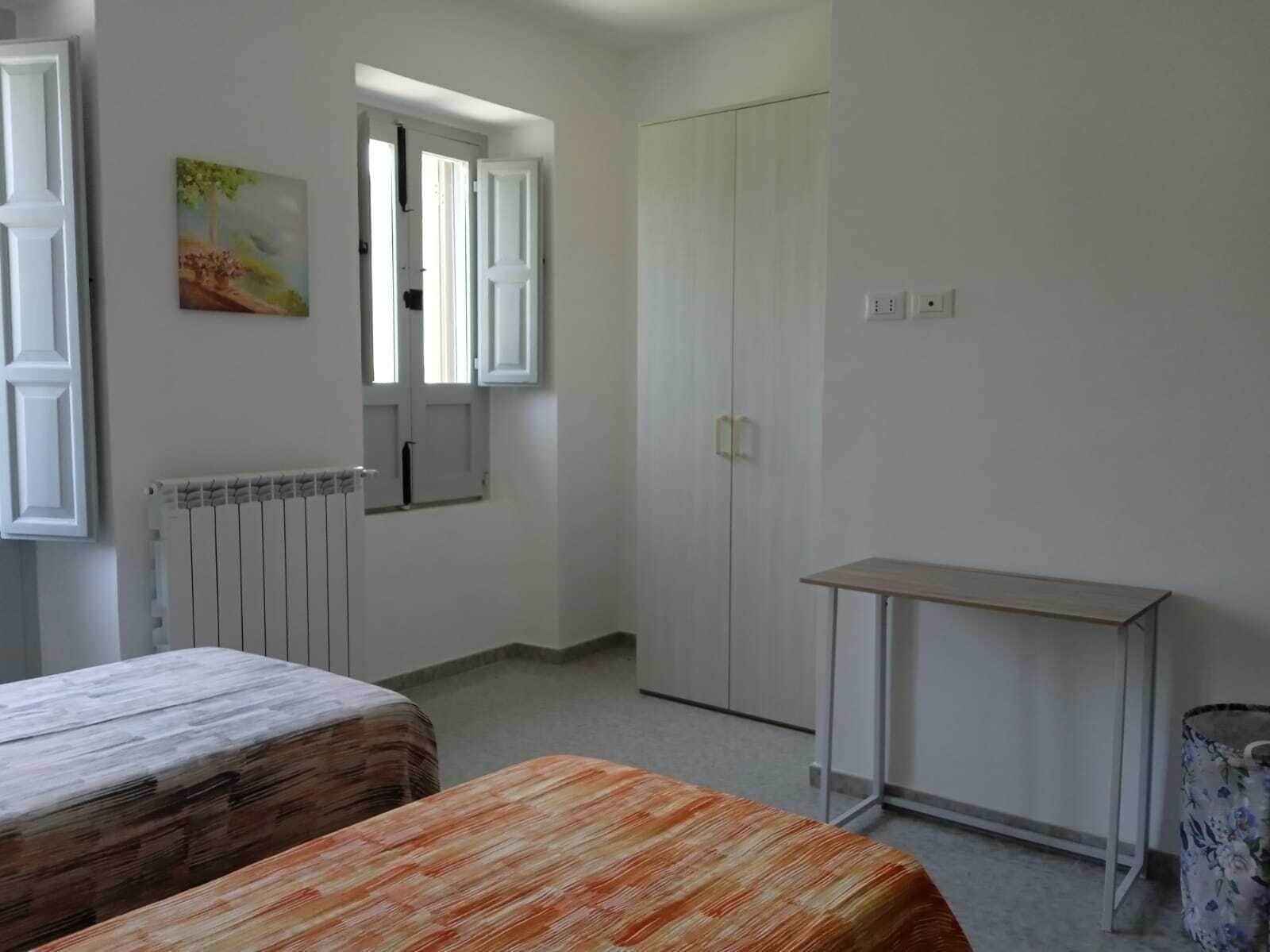 A room with a bed, a table, a wardrobe, a radiator, and a painting on the wall.