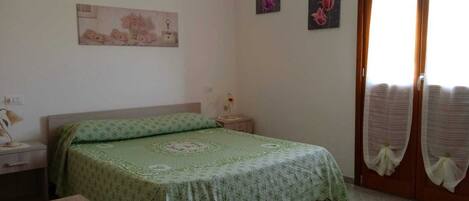Un dormitorio con una cama, una mesita de noche, una mesa de madera y una puerta con cortinas.