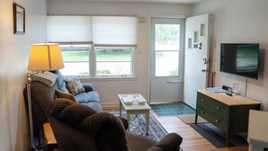 A living room with a sofa, a coffee table, a lamp, a TV, and a door leading outside. - Viola Suite #2 | Quiet 2BR, Lg Yard, 3 Mi to Mayo! (Rochester)