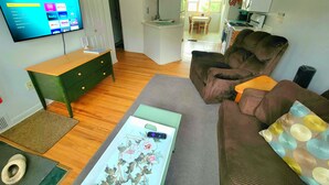 A living room with a TV, a sofa, a coffee table, and a kitchen in the background. - Viola Suite #2 | Quiet 2BR, Lg Yard, 3 Mi to Mayo! (Rochester)