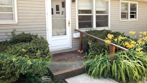 A two-story house with a front door, a small porch, and a wooden staircase leading to the entrance. - Viola Suite #2 | Quiet 2BR, Lg Yard, 3 Mi to Mayo! (Rochester)