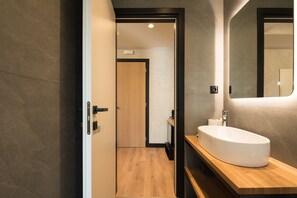 Ein modernes Badezimmer mit einem hölzernen Waschtisch, einer großen weißen Spüle und einem Spiegel darüber.