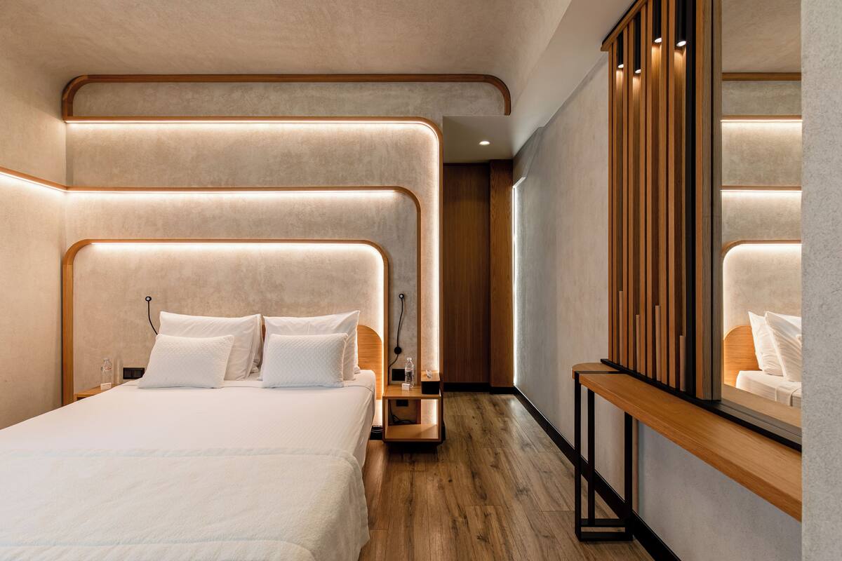 Une chambre d’hôtel moderne avec un grand lit, des tables de chevet, un miroir et un plancher en bois.