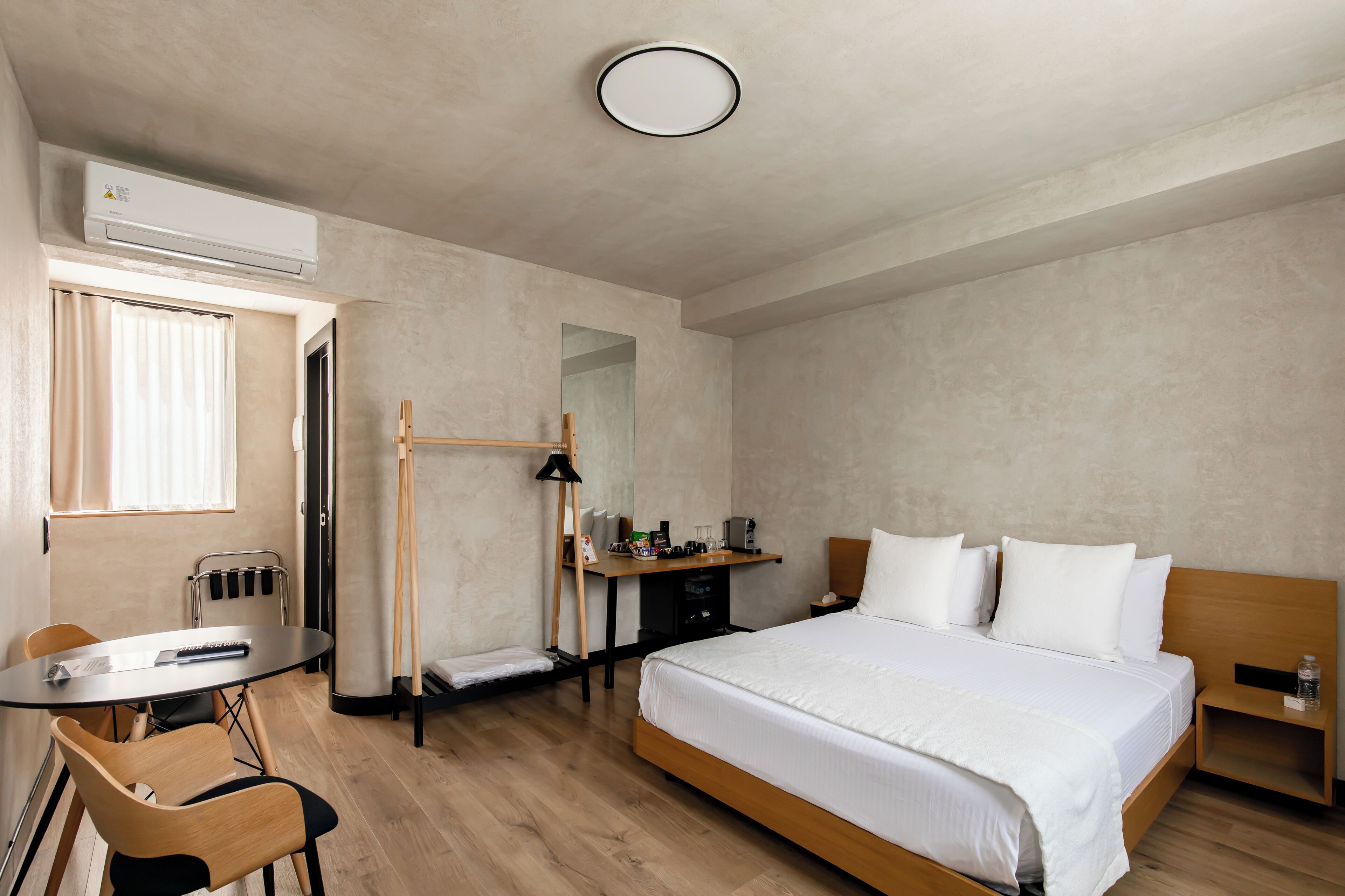 Hotellihuone, jossa on sänky, työpöytä, tuoli, pöytä ja ilmastointilaite.