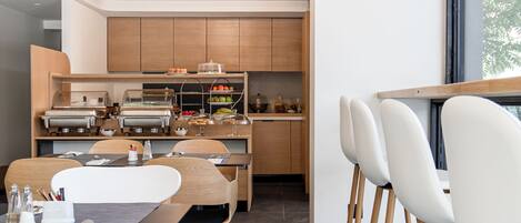 A modern kitchen with built-in appliances, wooden cabinets, and a dining area with white chairs and a black table.