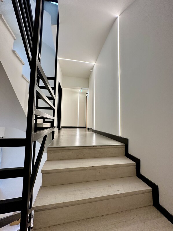 Eine moderne Treppe mit Metallgeländer, die zu einer Zwischenebene mit einer Tür führt.