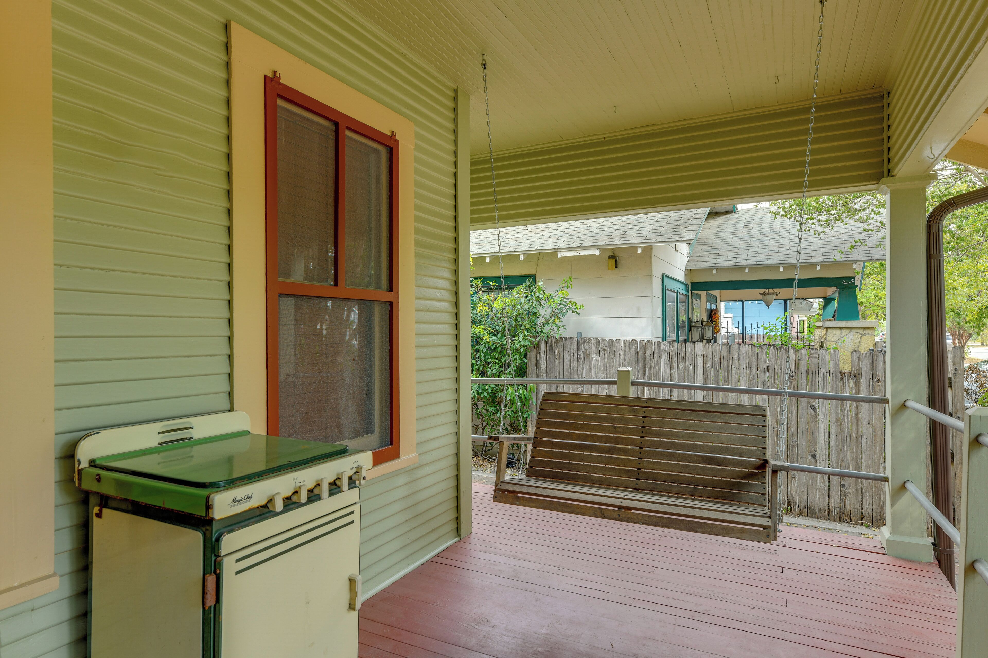 A covered porch with a vintage stove, a bench, and a wooden fence in the background.