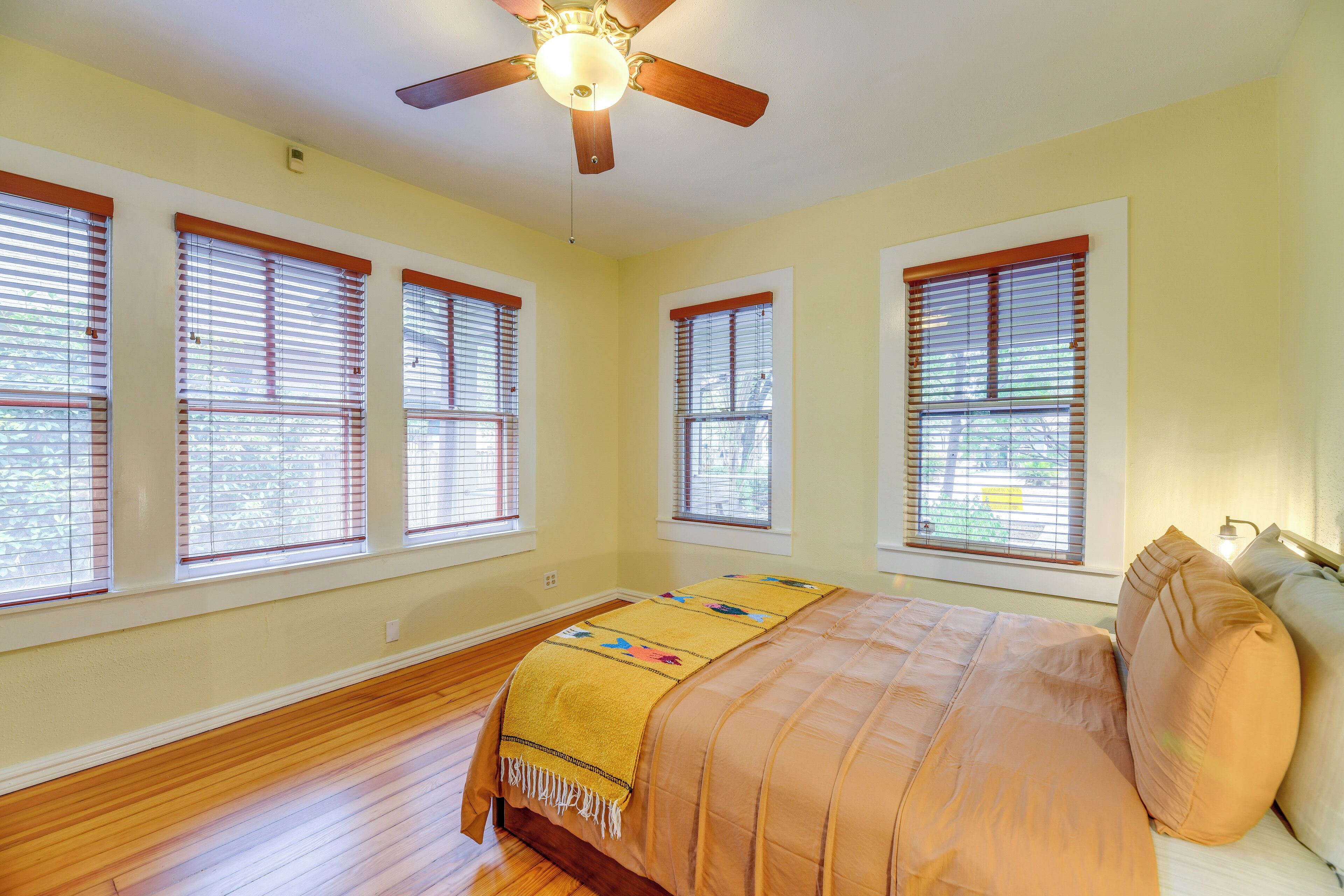 Un dormitorio con cama, piso de madera y ventanas amplias con persianas.