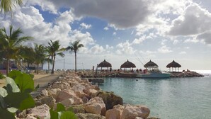 A beachside resort with a wooden walkway, palm trees, and thatched-roof structures. - Blue Bay Beach Apartments (Sint Michiel)