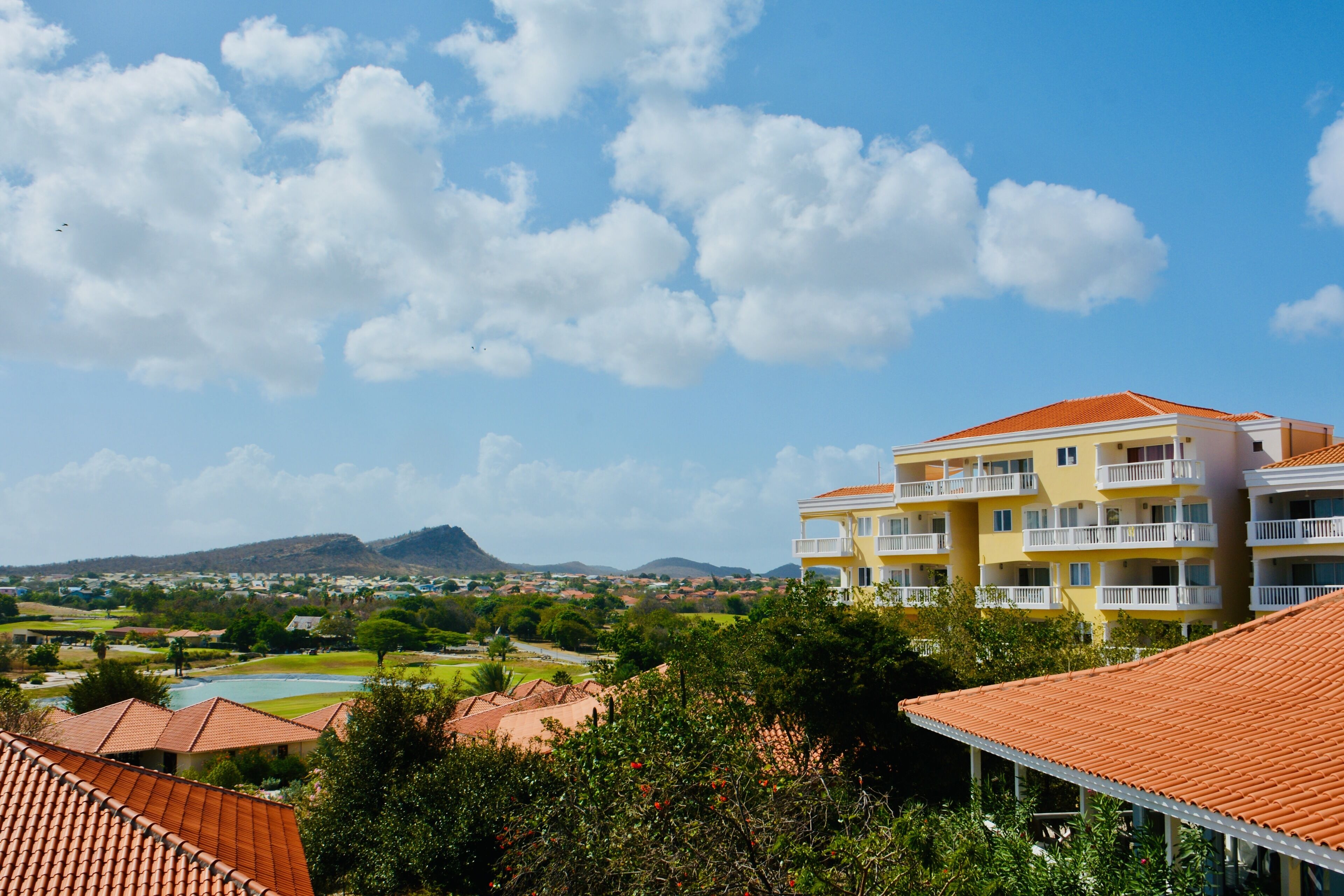 Ein Hotel mit rotem Ziegeldach, mehreren Balkonen und Blick auf eine Berglandschaft.