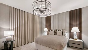 Un dormitorio moderno con una cama grande, dos mesitas de noche con lámparas, una araña y paneles de madera en las paredes.