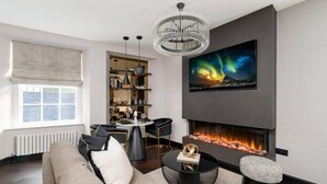 Una sala de estar moderna con chimenea, un candelabro y un televisor grande mostrando las auroras boreales.