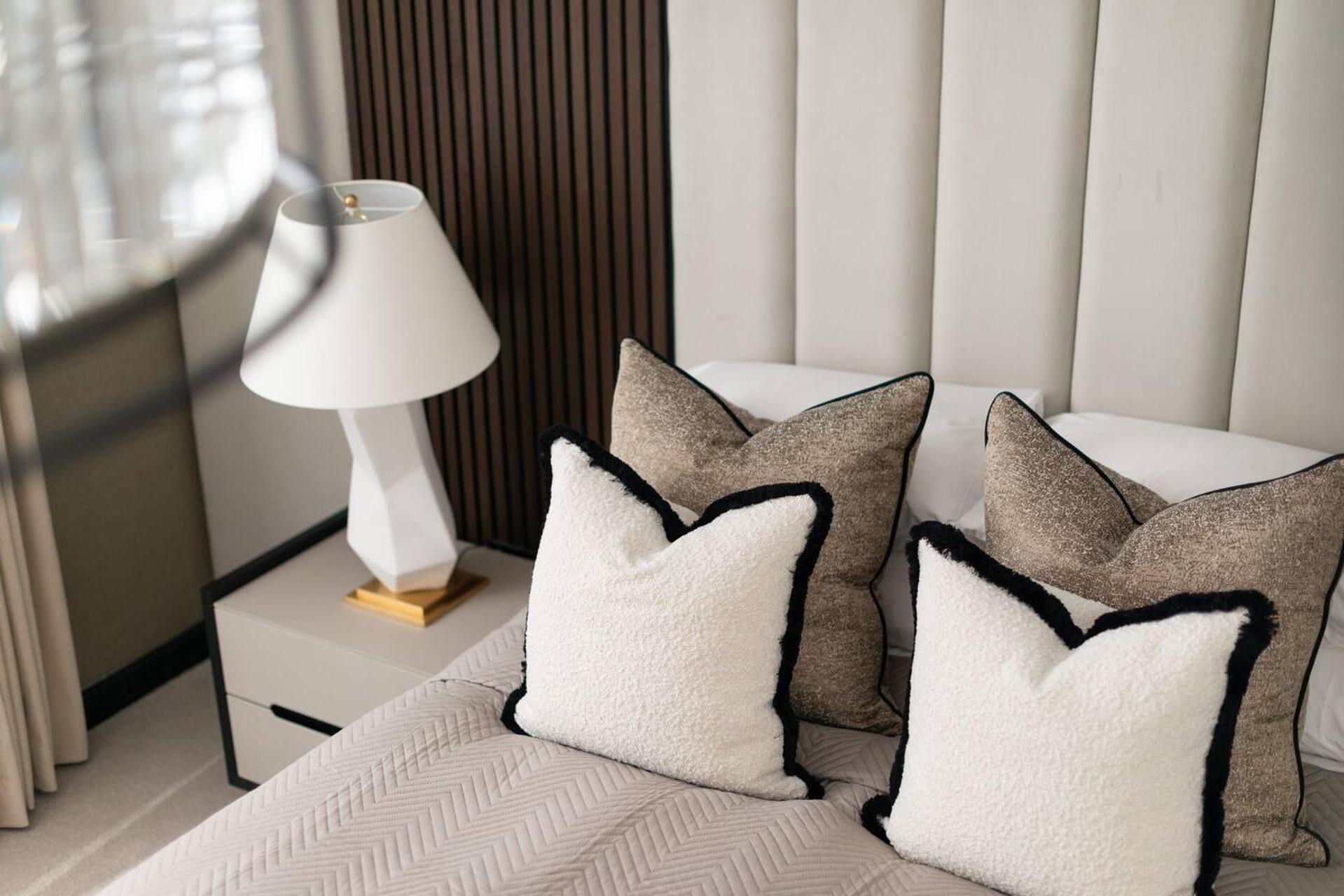 A neatly made bed with a patterned bedspread and several pillows with black trim.