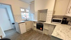 A compact kitchen with white cabinets, a built-in oven, a microwave, and a dishwasher. - Essex 2-bed House nr Stanstead With Arcade Machine (Braintree)