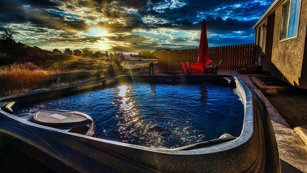 A hot tub with a wooden deck, surrounded by a wooden fence and a house.