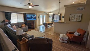 A living room with a sofa, armchair, ottoman, TV, and a dining area with a table and chairs.