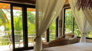 A bedroom with a large bed, a wicker chair, and a view of palm trees through the windows. - BEACHFRONTGEM- owner’s villa-expansive endless beach. Amazing Sept Oct discounts (Savegre)
