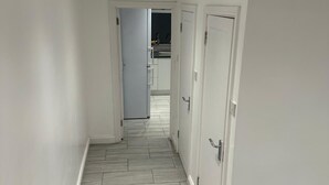 A hallway with a tiled floor, white walls, and doors leading to a kitchen area. - Kuramoh Modern Apartment (London)