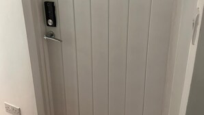 A white door with a modern lock and a small electronic device mounted on the wall beside it. - Kuramoh Modern Apartment (London)