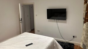 A bedroom with a bed, a TV mounted on the wall, a remote control on the bed, and a door leading to another room. - Kuramoh Modern Apartment (London)