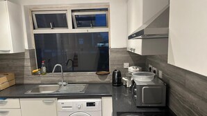 A modern kitchen with a built-in washer, a sink, a kettle, and a microwave. - Kuramoh Modern Apartment (London)