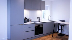 A modern kitchen with grey cabinets, a built-in oven, a sink, and a small dining area with a chair. - Thout Seaview Luxury Apartment (London)