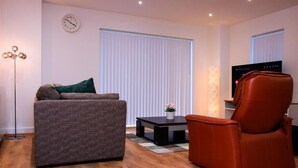 A modern living room with a grey sofa, a red armchair, a small coffee table, and a TV. - Thout Seaview Luxury Apartment (London)