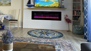 Ein Wohnzimmer mit Wandfernseher, Kamin, maritimer Dekoration und Bücherregal.