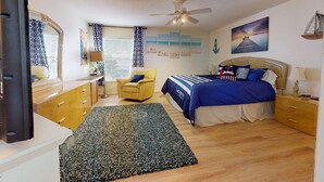 Ein Schlafzimmer mit Bett, Stuhl, Schreibtisch, Spiegel und Deckenventilator.