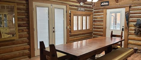 A log cabin interior with a wooden dining table, benches, and a ceiling fan.