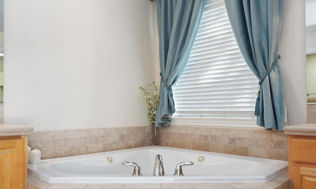 Een badkamer met een vrijstaand bad, een raam met blauwe gordijnen, en een decoratieve plant.