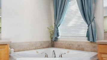 Een badkamer met een vrijstaand bad, een raam met blauwe gordijnen, en een decoratieve plant.