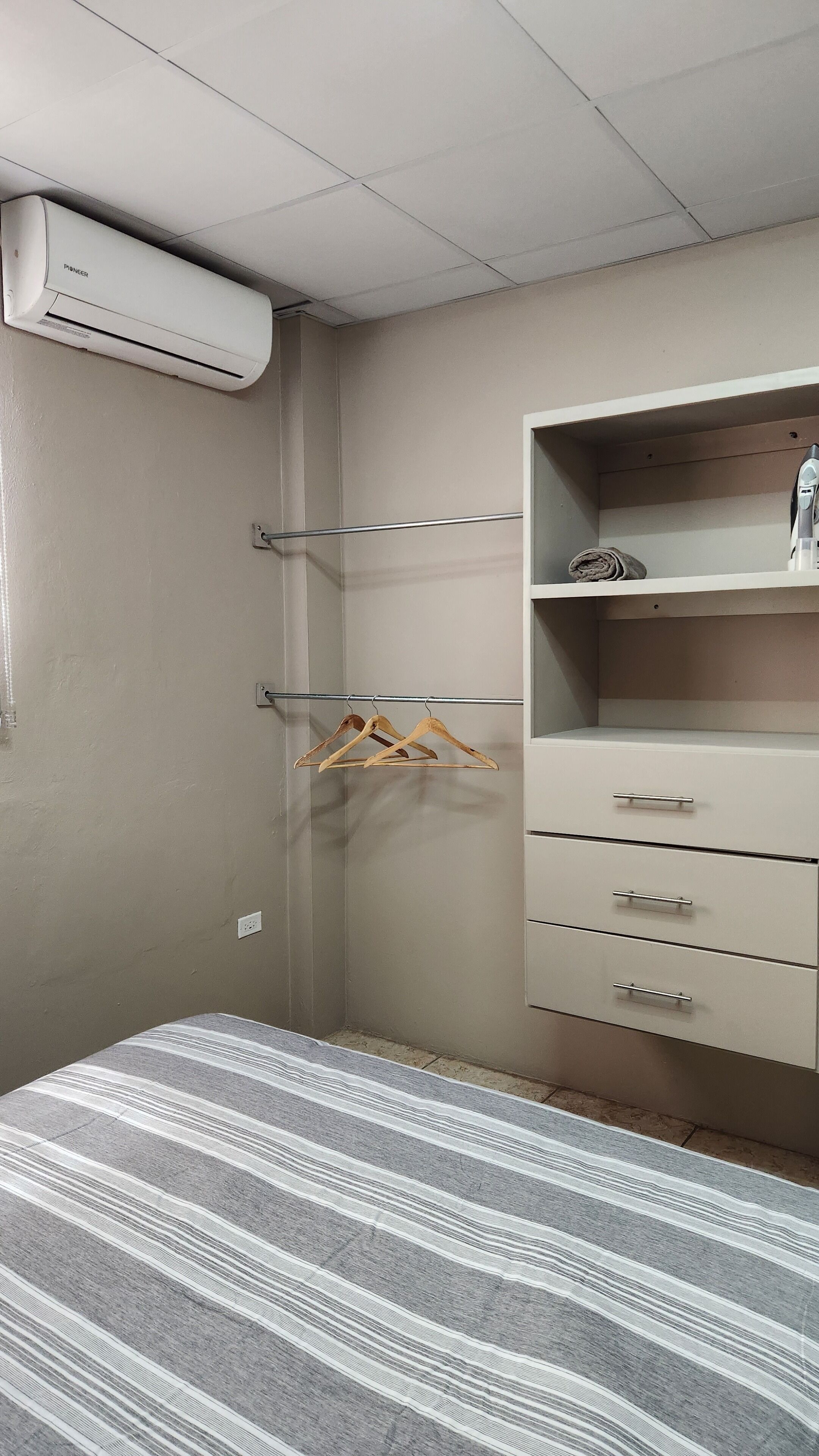 Ein Schlafzimmer mit Bett, Kleiderschrank, Kleiderstange und Klimaanlage.