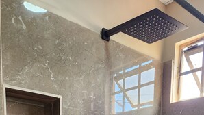 Ein Badezimmer mit dunklen Marmorfliesen, einer Dusche inklusive schwarzem Duschschlauch und einem Fenster mit Gittermuster.