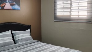 Ein Schlafzimmer mit einem Bett, einem Fenster mit Jalousien, einer Deckenleuchte und einem Wandbild.